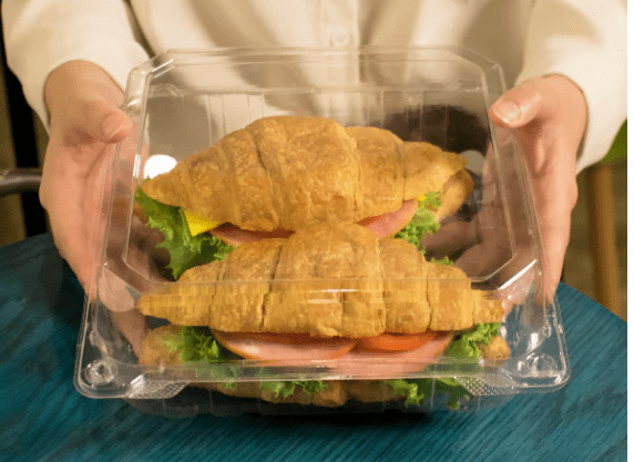 Hands holding container with two croissant sandwiches